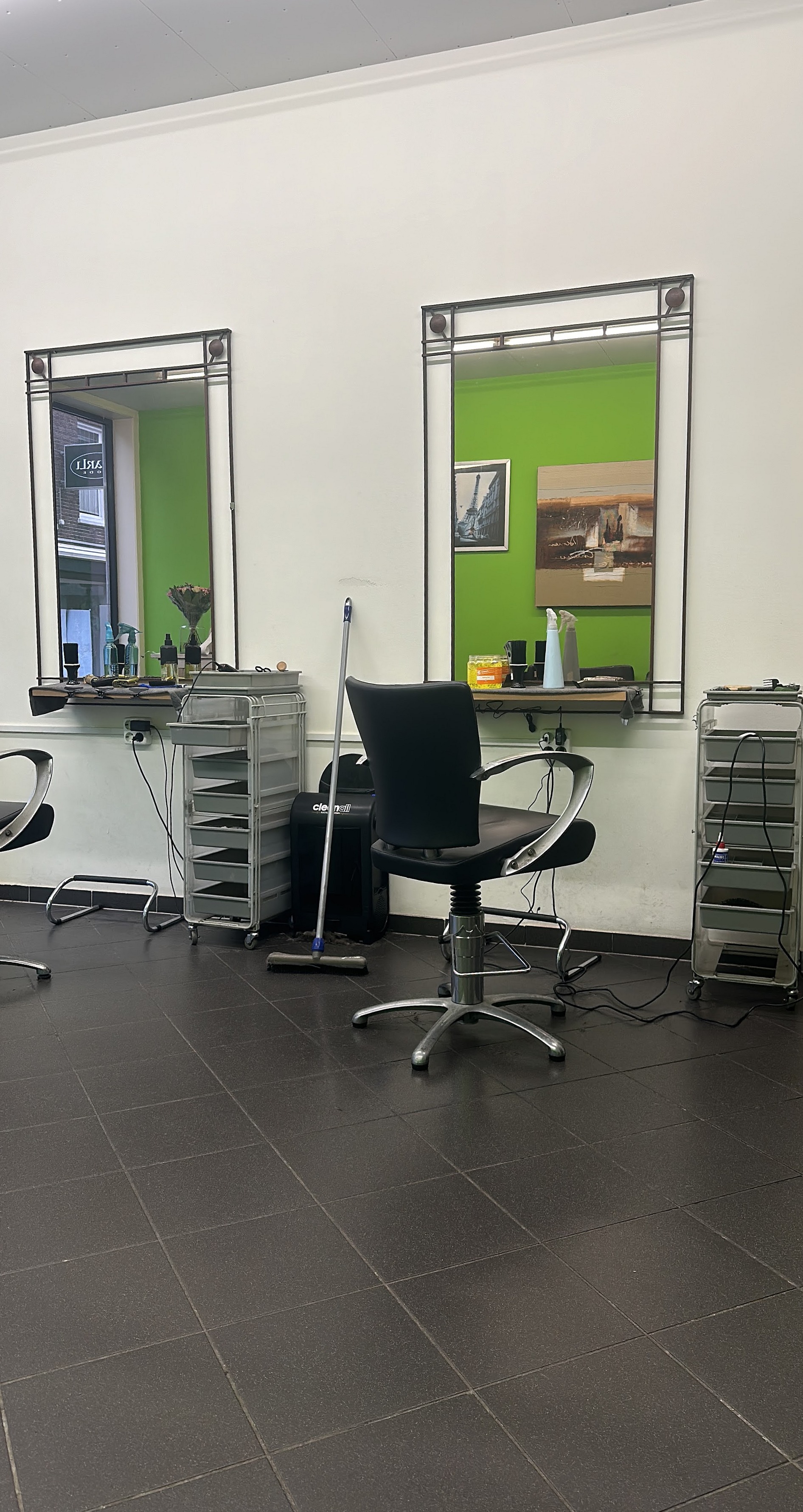 Een knipplek bij Kapsalon Castal: twee spiegels tegen de witte en groene muur, een zwarte kappersstoel en de grijze tegelvloer